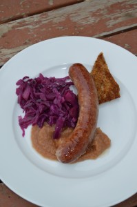 A plate of sausage, toast, apple sauce, and braised red cabbage.