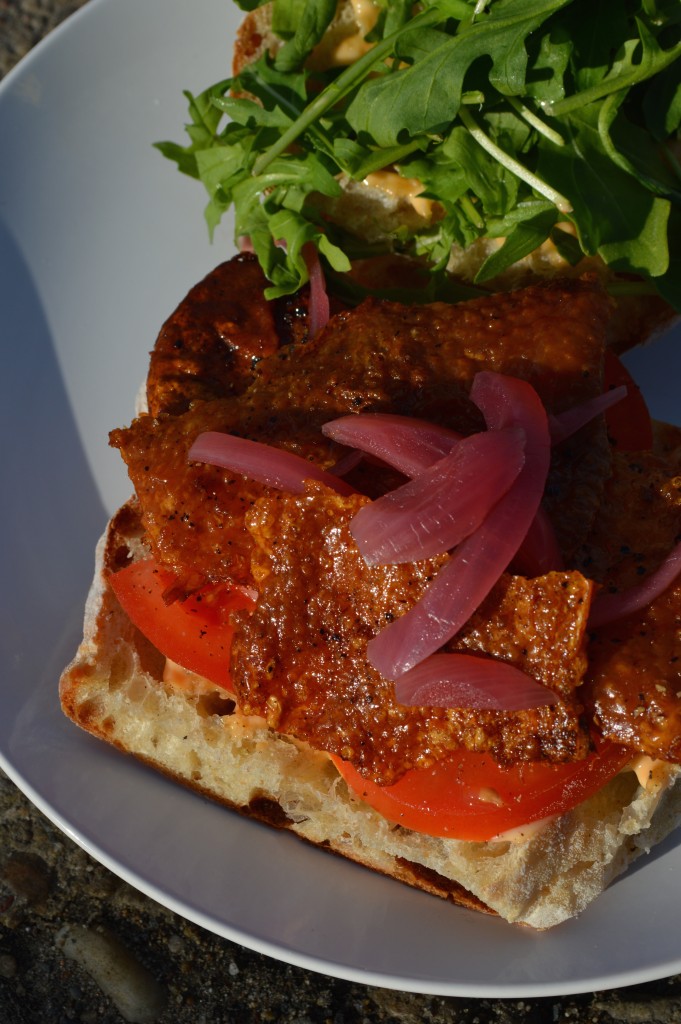 A sandwich made with tomato, chili mayo, pickled onion, and crispy chicken skin.