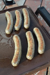 Breakfast sausages frying on a griddle.