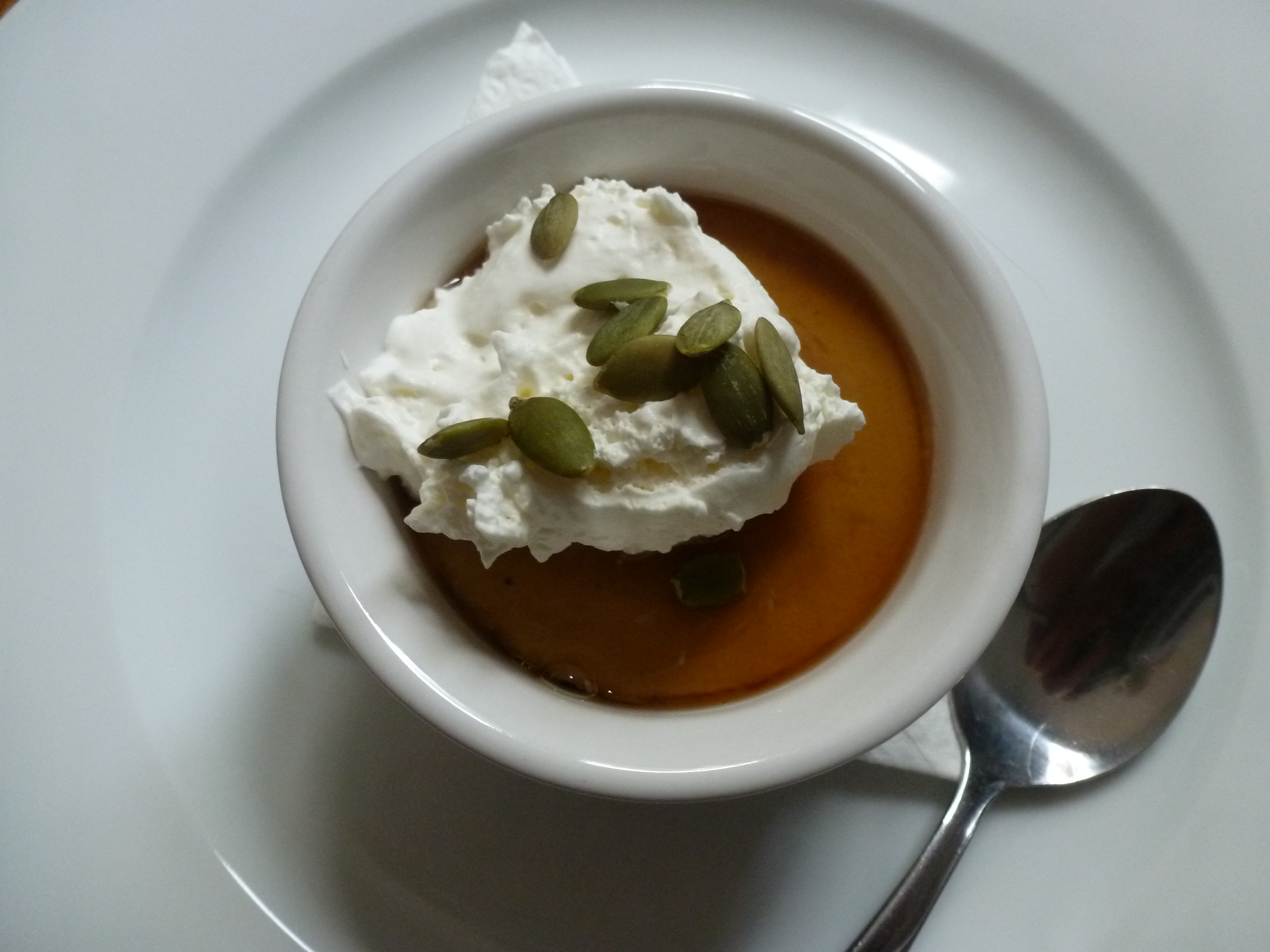 Pumpkin custard, baked into a ramekin, served with whipped cream, maple syrup, and pumpkin seeds