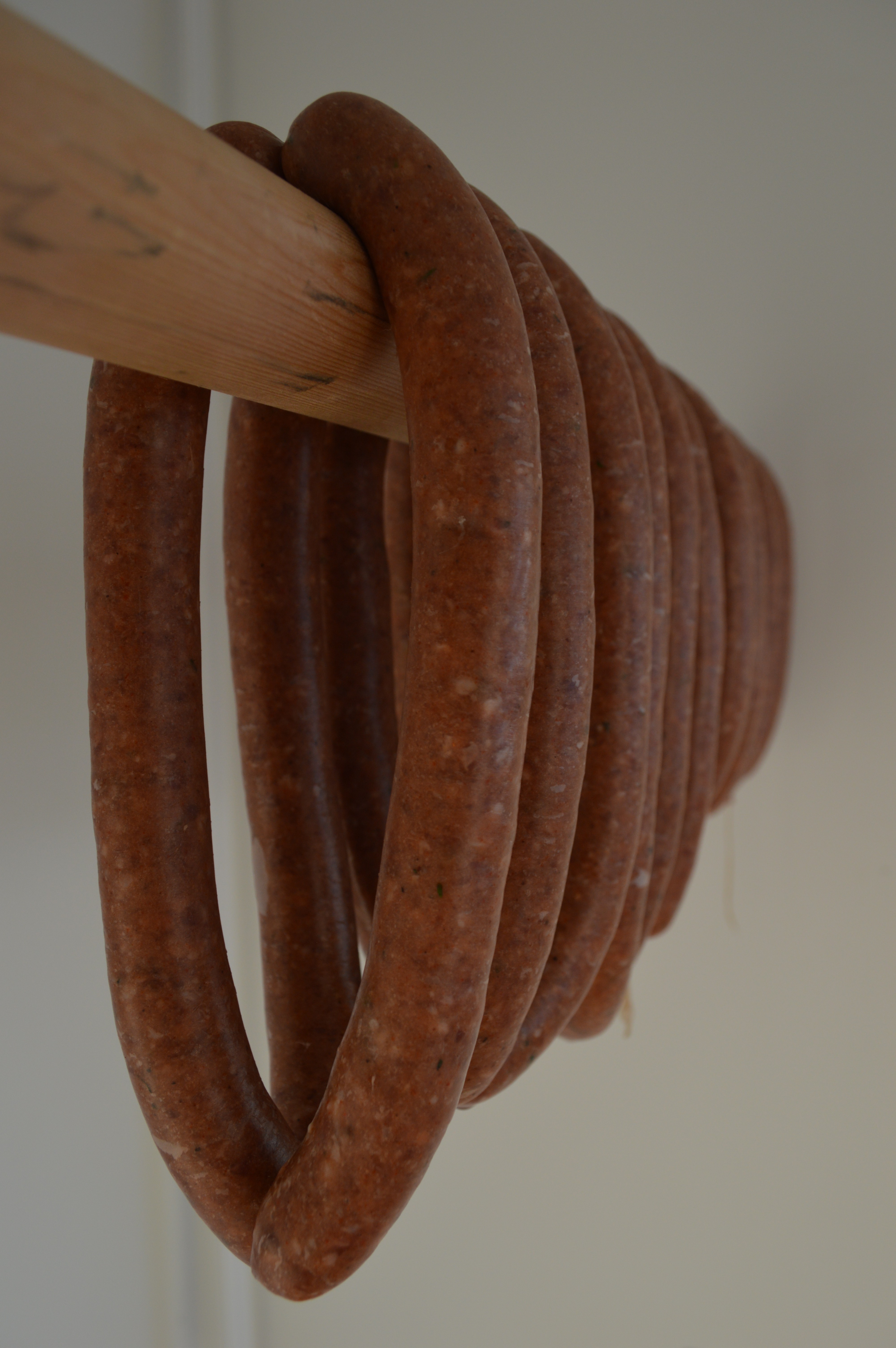 Spicy lamb sausages hanging on a wooden dowel.