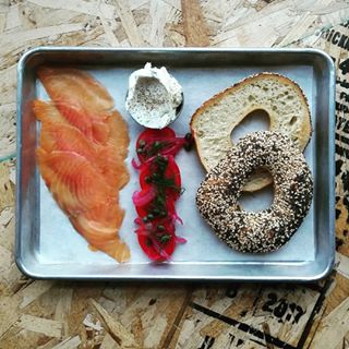A platter of cured salmon, bagel, cream cheese, and vegetables.